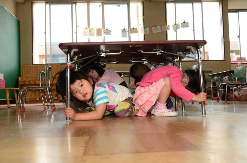 地震が発生したことを想定した訓練で机の下に避難する園児たち
